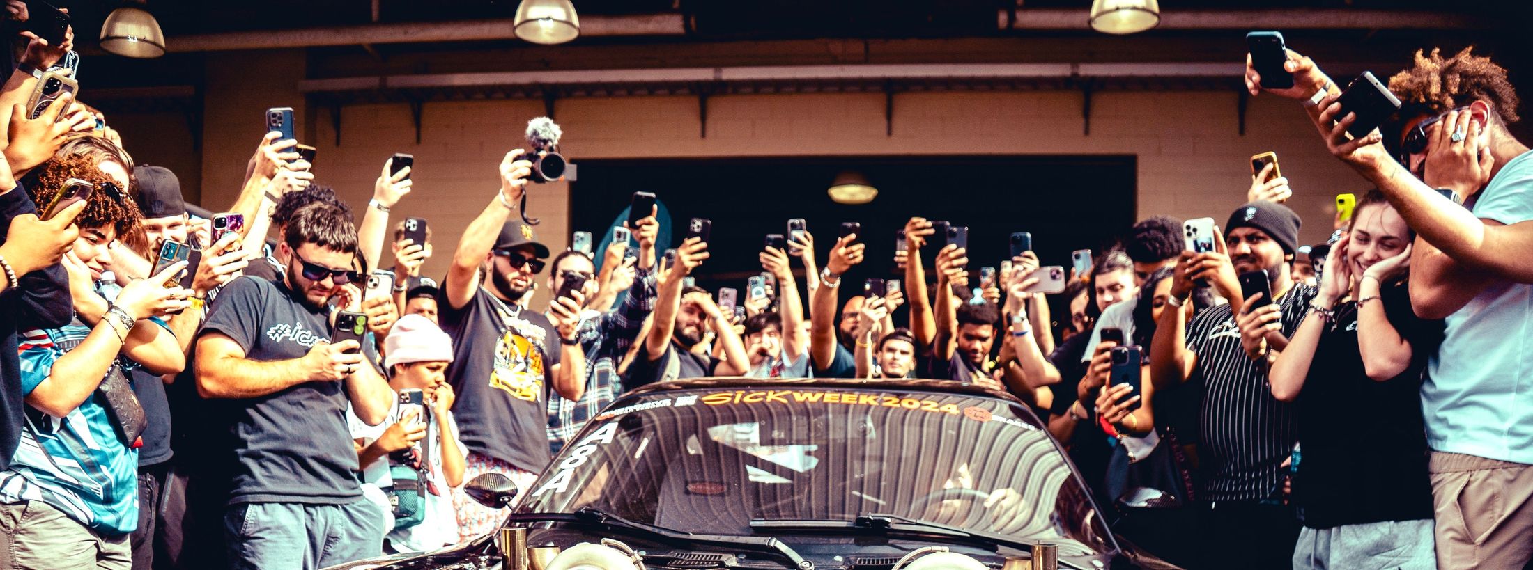 A crowd photographing a car reveal, dozens of phones raised